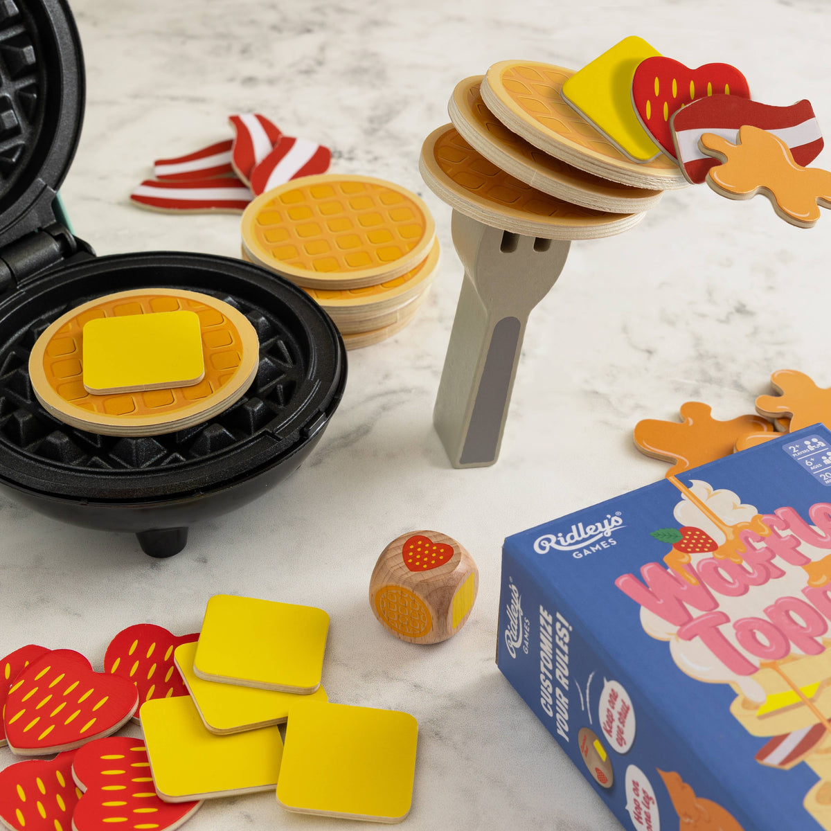 Waffle Topple board game by Chronicle Books featuring colorful waffle-themed pieces and game components on a white background.