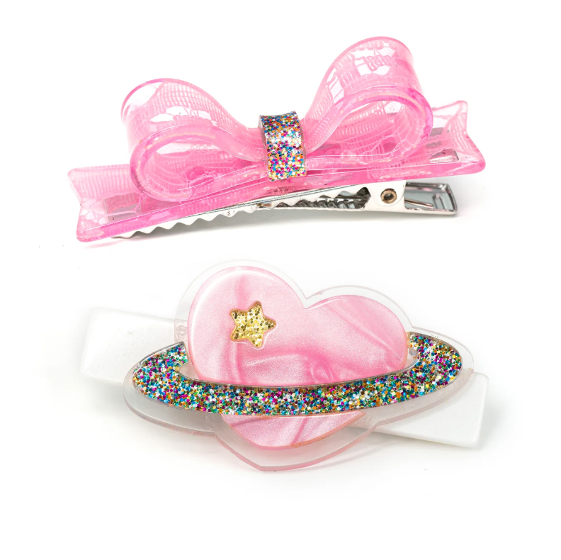 Pink heart-shaped planet hair clip with bow and pearl accents by Lilies & Roses NY, featuring a shiny, pearlized finish.