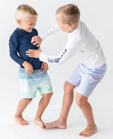 Baby boy wearing navy long sleeve rash guard by RuffleButts and RuggedButts, showing the blue sun protection swim shirt.