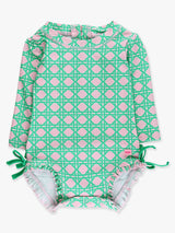 Baby girl in pink coastal cane long-sleeve rash guard swimsuit with signature rear ruffles, by RuffleButts and RuggedButts.