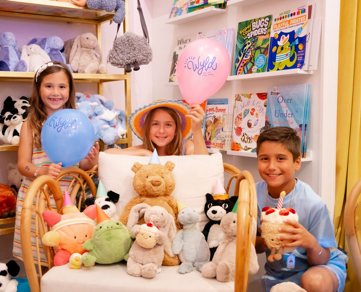 Three kids with Wyld balloons and Jellycat friends in party hats