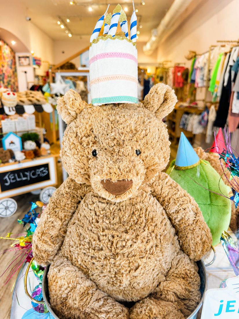 Giant Jellycat bear wearing a party hat with a birthday cake